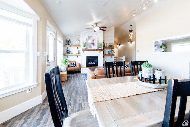 dining area featuring a large fireplace, wood finished floors, a ceiling fan, baseboards, and vaulted ceiling