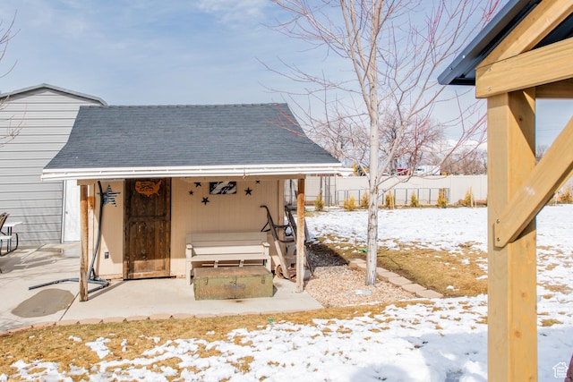 snow covered patio with fence and an outdoor structure