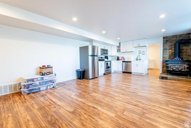 kitchen featuring light wood finished floors, visible vents, a wood stove, stainless steel appliances, and white cabinetry