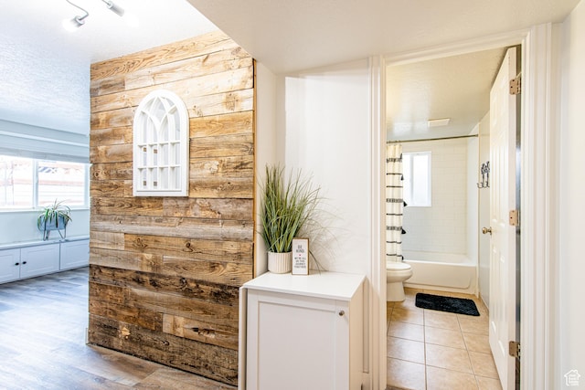bathroom featuring wooden walls, toilet, shower / tub combo with curtain, tile patterned flooring, and a textured ceiling