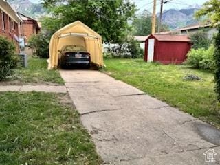 1105 9th St, Ogden, UT 84404 - view of grassy yard featuring a storage unit, a detached carport, an outdoor structure, driveway, and a mountain view
