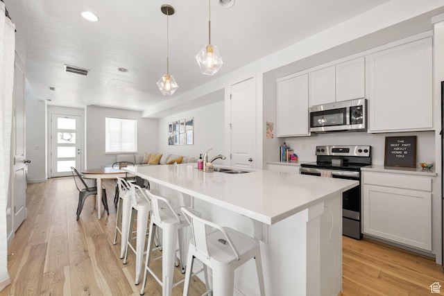 kitchen featuring appliances with stainless steel finishes, open floor plan, a sink, and light wood-style flooring