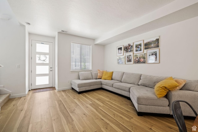 living room with a textured ceiling, light wood-style flooring, visible vents, baseboards, and stairway