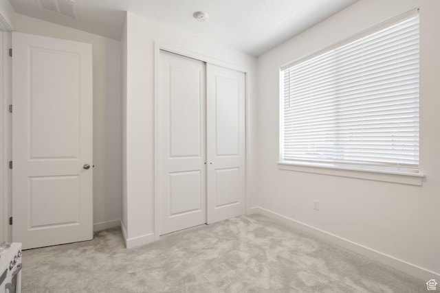 unfurnished bedroom with light carpet, a closet, visible vents, and baseboards