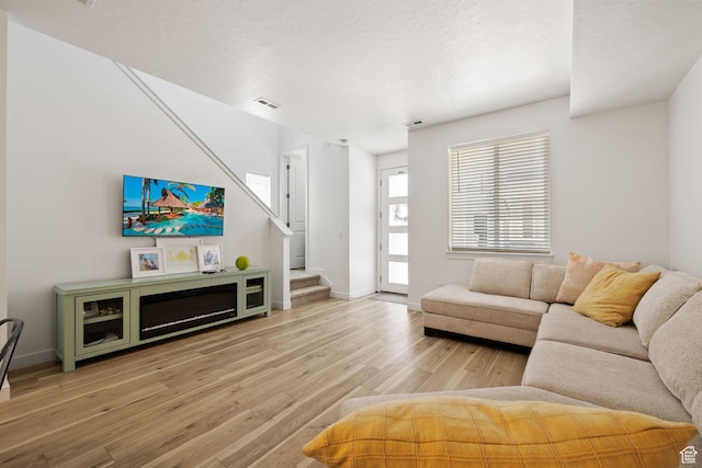 living room featuring stairs, light wood finished floors, visible vents, and baseboards