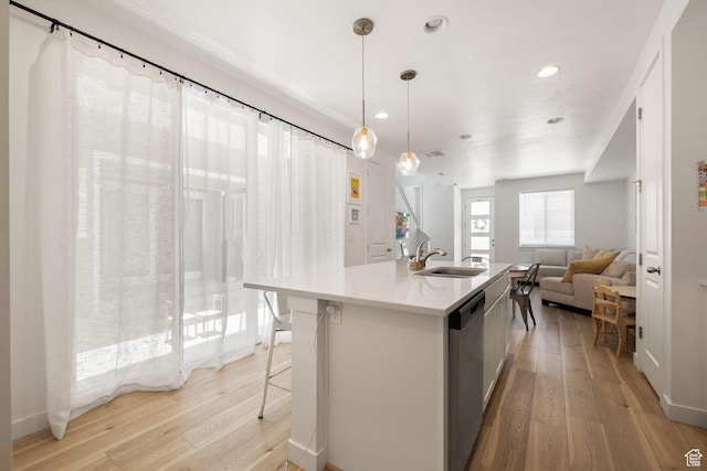 kitchen with a sink, light wood-style floors, light countertops, stainless steel dishwasher, and an island with sink