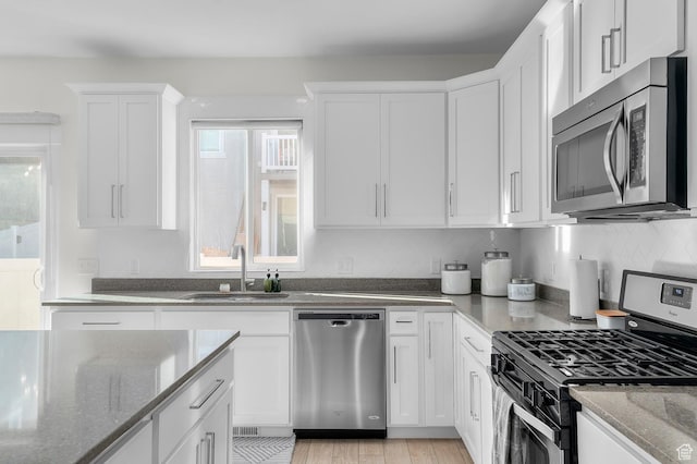 4927 W Yellow Topaz Dr, Herriman, UT 84096 - kitchen featuring a sink, white cabinetry, appliances with stainless steel finishes, dark stone counters, and light wood finished floors