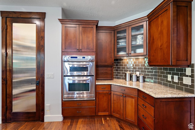 267 E Lucky Star Way, Farmington, UT 84025 - kitchen with double oven, dark wood-style floors, decorative backsplash, glass insert cabinets, and light stone counters