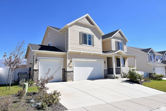 view of front facade featuring a porch, fence, a garage, stone siding, and driveway