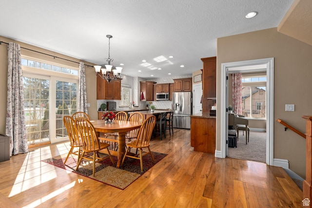 dining space with a chandelier, light wood-style floors, plenty of natural light, baseboards, and a textured ceiling