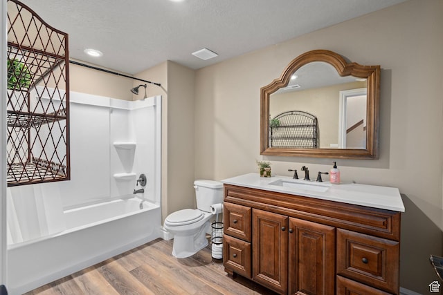 full bath featuring wood finished floors, a textured ceiling, toilet, vanity, and bathtub / shower combination