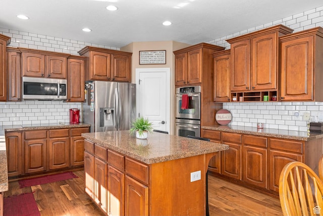 kitchen with appliances with stainless steel finishes, a center island, tasteful backsplash, dark wood-type flooring, and recessed lighting