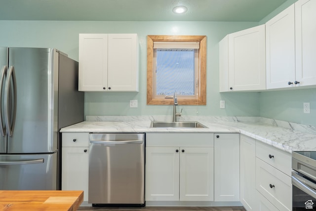 kitchen with white cabinets, light stone countertops, stainless steel appliances, and a sink
