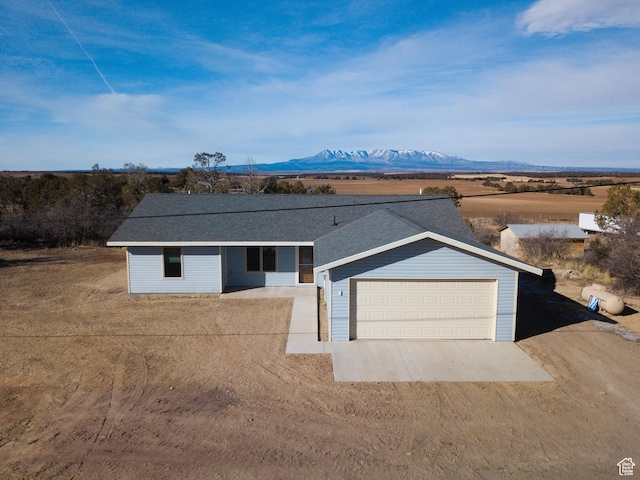 ranch-style home with driveway, a shingled roof, a garage, and a mountain view
