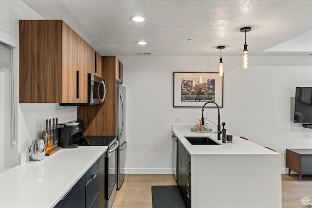 kitchen featuring brown cabinets, light countertops, appliances with stainless steel finishes, a sink, and a peninsula