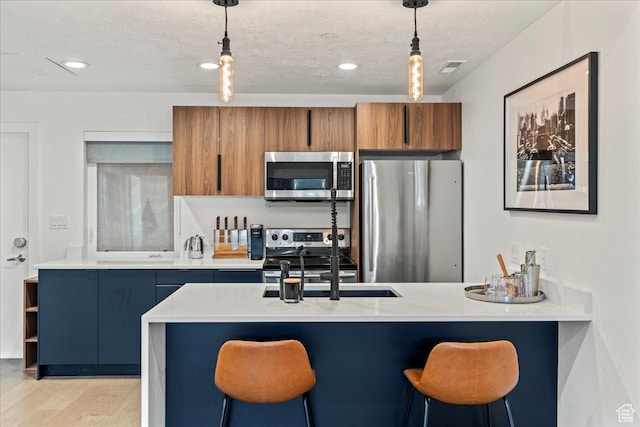 kitchen featuring a breakfast bar, light countertops, hanging light fixtures, appliances with stainless steel finishes, and brown cabinetry