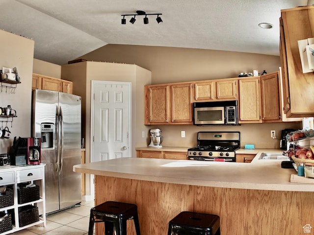 kitchen with light tile patterned floors, lofted ceiling, a peninsula, stainless steel appliances, and light countertops