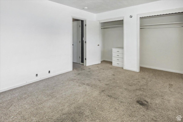 unfurnished bedroom featuring carpet floors, baseboards, and two closets