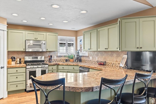 1004 W 4050 S, Riverdale, UT 84405 - kitchen featuring light wood-style flooring, a peninsula, a kitchen breakfast bar, green cabinets, and appliances with stainless steel finishes