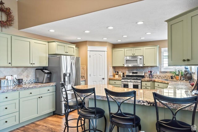 1004 W 4050 S, Riverdale, UT 84405 - kitchen with stainless steel appliances, a peninsula, a sink, green cabinets, and light wood finished floors