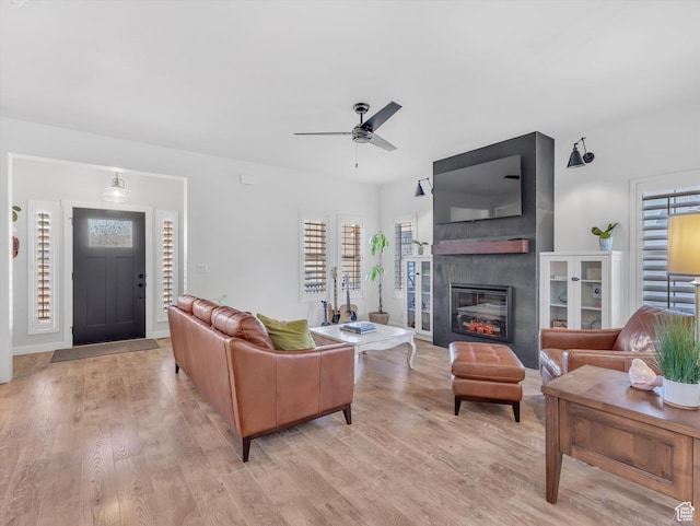living room with a ceiling fan, a large fireplace, light wood-style flooring, and baseboards