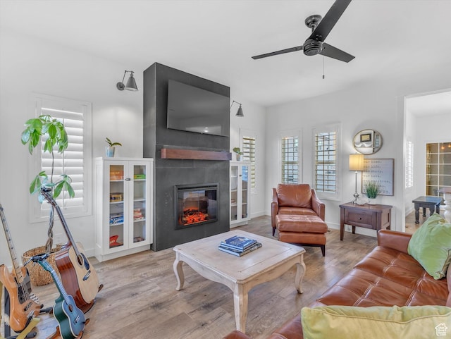 living area featuring baseboards, a ceiling fan, wood finished floors, and a glass covered fireplace