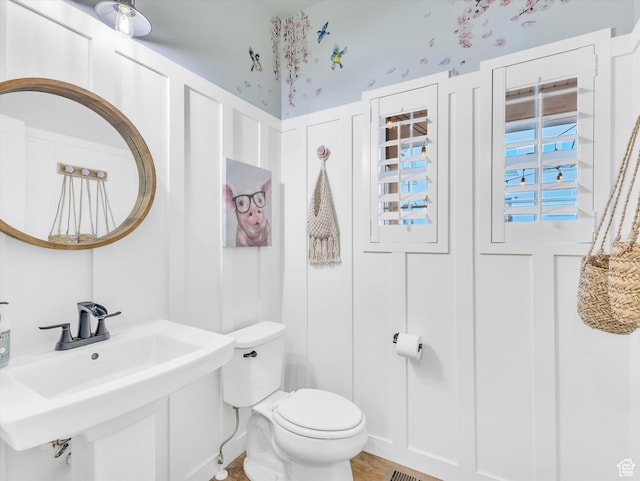bathroom featuring toilet, a decorative wall, and a sink