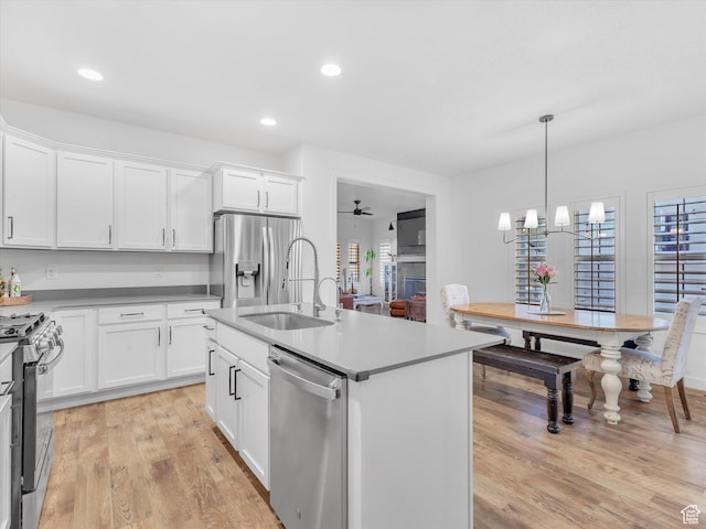kitchen with light wood finished floors, white cabinets, appliances with stainless steel finishes, a sink, and ceiling fan with notable chandelier