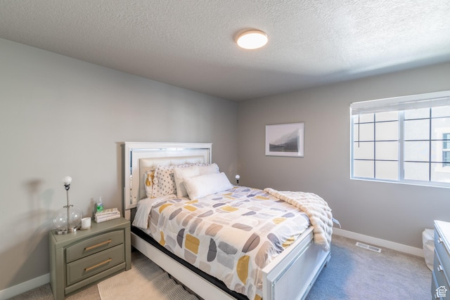 bedroom with light carpet, a textured ceiling, visible vents, and baseboards