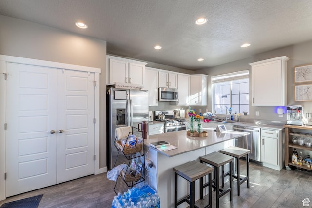 kitchen featuring a breakfast bar area, stainless steel appliances, recessed lighting, white cabinets, and wood finished floors