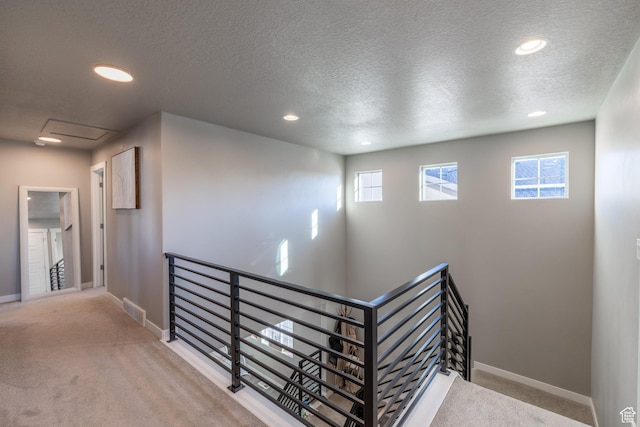 hallway featuring carpet, visible vents, attic access, an upstairs landing, and baseboards
