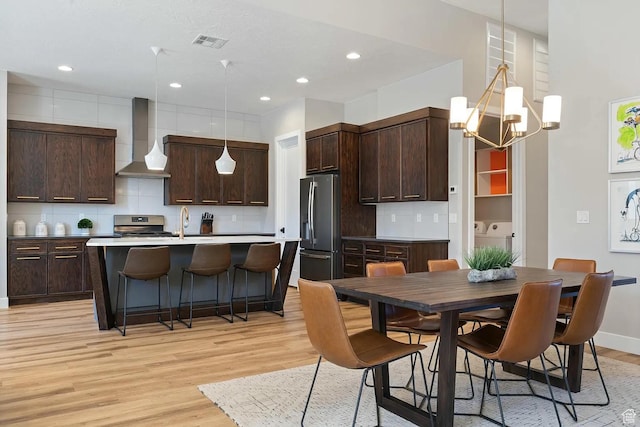 5417 W Copper Cliffs Way, Hurricane, UT 84737 - kitchen featuring light wood-style flooring, stainless steel appliances, washing machine and clothes dryer, visible vents, and wall chimney exhaust hood