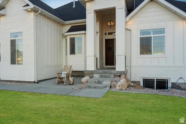 entrance to property featuring board and batten siding, brick siding, a lawn, and visible vents
