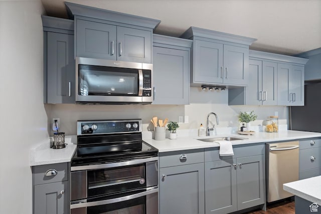 kitchen with dark wood-style floors, gray cabinets, stainless steel appliances, light countertops, and a sink