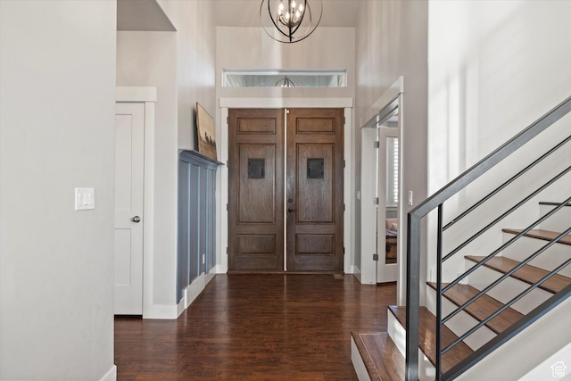 foyer entrance featuring a towering ceiling, an inviting chandelier, wood finished floors, baseboards, and stairs