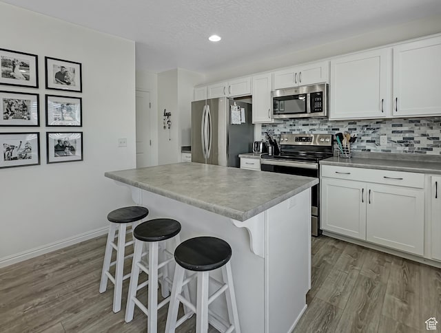 2095 W 3330 S, Syracuse, UT 84075 - kitchen featuring appliances with stainless steel finishes, wood finished floors, a kitchen breakfast bar, white cabinetry, and a textured ceiling