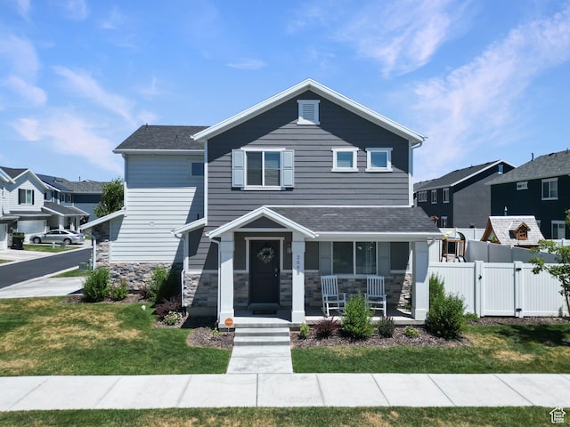 view of front of house featuring a porch, a front yard, a gate, fence, and stone siding