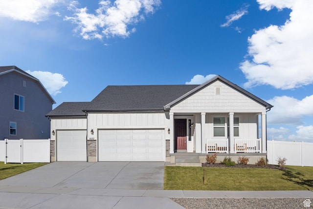 view of front of house featuring a porch, an attached garage, fence, a front lawn, and board and batten siding
