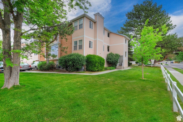 view of side of home featuring entry steps, fence, a chimney, and a lawn