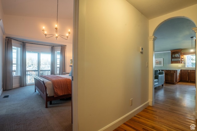 hallway featuring vaulted ceiling, a chandelier, wood finished floors, baseboards, and arched walkways