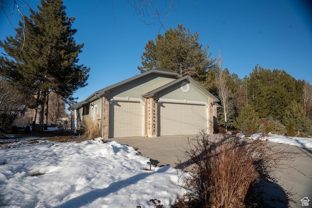 snow covered property with brick siding, driveway, a garage, and stucco siding