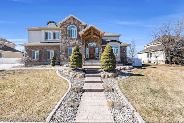 view of front of home featuring stone siding, a front yard, fence, and stucco siding