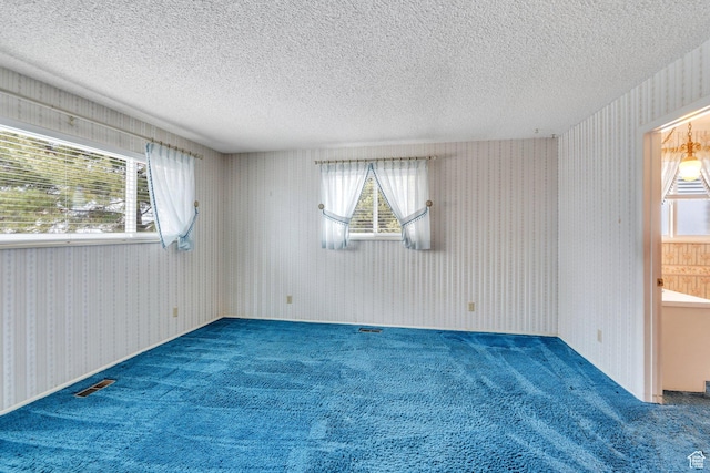 unfurnished room featuring a healthy amount of sunlight, wallpapered walls, and a textured ceiling