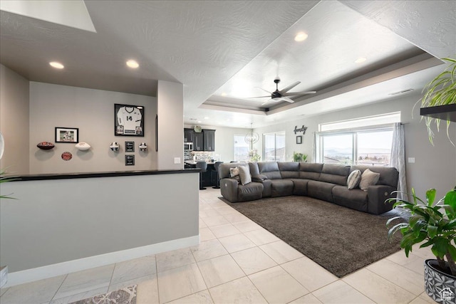 living room with a textured ceiling, a raised ceiling, a ceiling fan, and baseboards