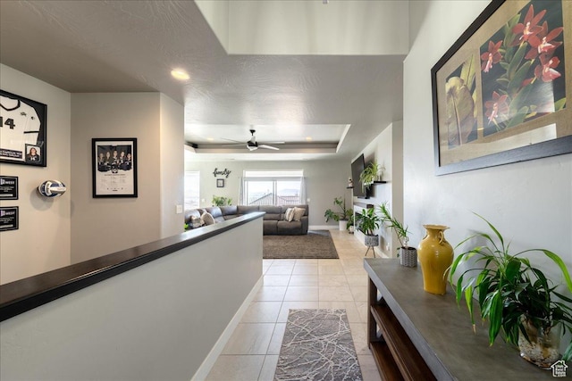 hallway featuring a raised ceiling, a textured ceiling, baseboards, and light tile patterned floors