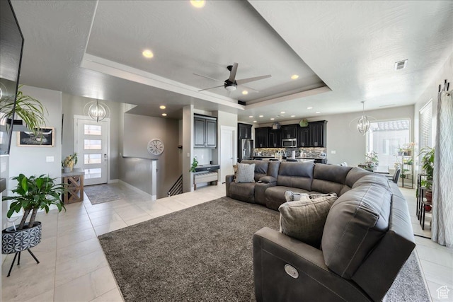 living room featuring a textured ceiling, light tile patterned flooring, ceiling fan with notable chandelier, visible vents, and a tray ceiling