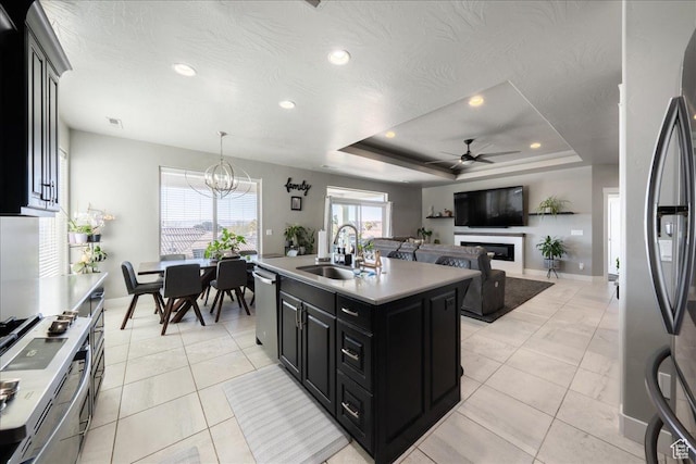 kitchen with appliances with stainless steel finishes, a tray ceiling, dark cabinetry, a fireplace, and a sink