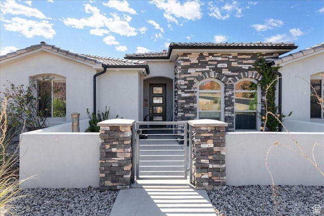 mediterranean / spanish house with stone siding, a fenced front yard, a tiled roof, a gate, and stucco siding