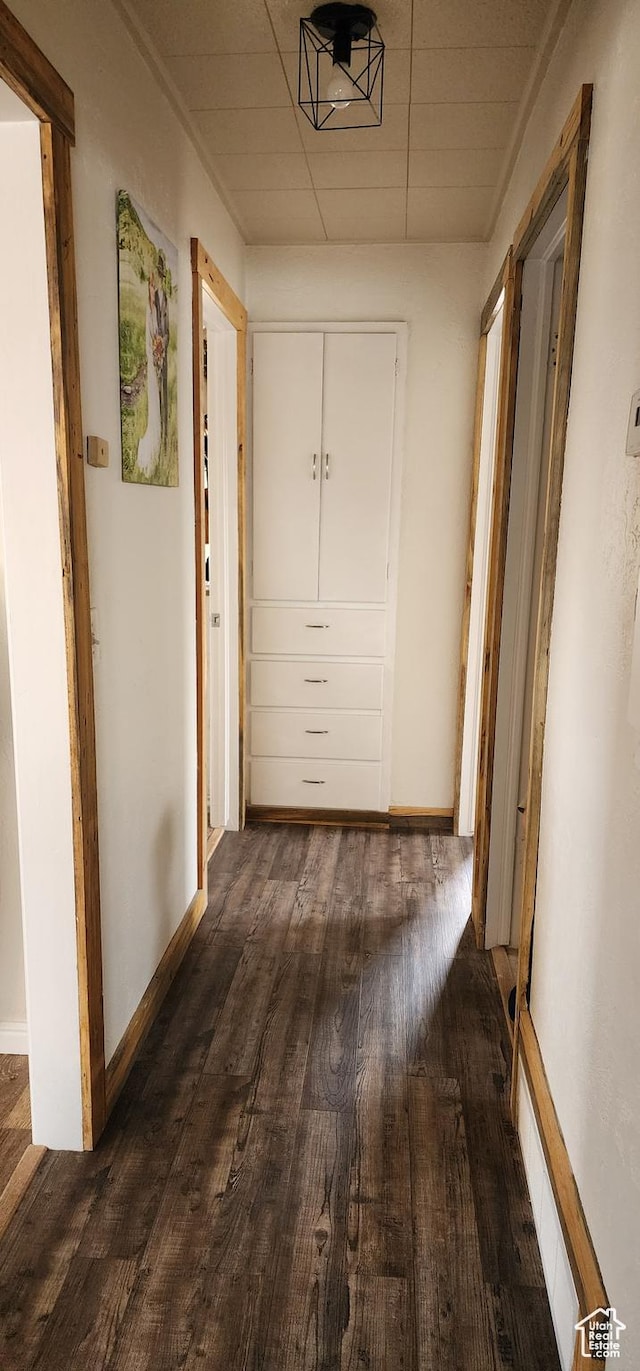 hallway with dark wood-type flooring, baseboards, and a paneled ceiling