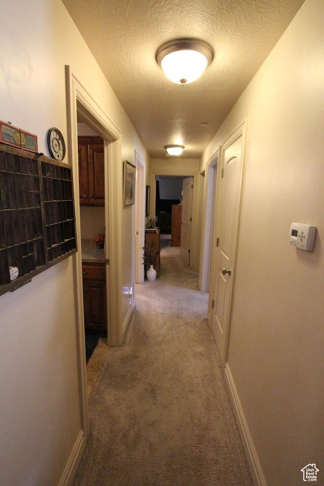 hallway featuring baseboards, a textured ceiling, and light colored carpet